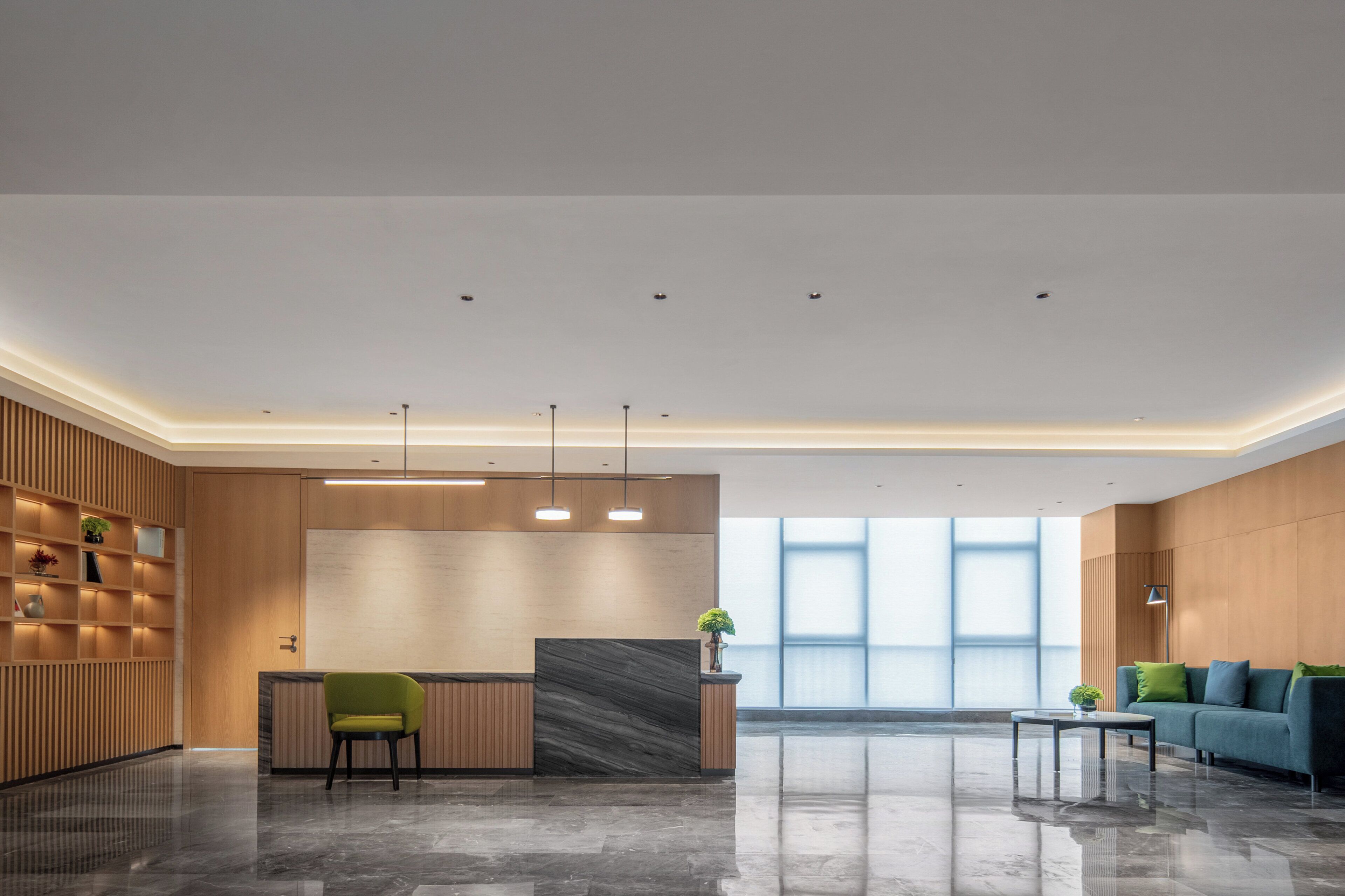 Un área de recepción moderna con mostrador, una silla verde, un sofá y una planta en maceta.
