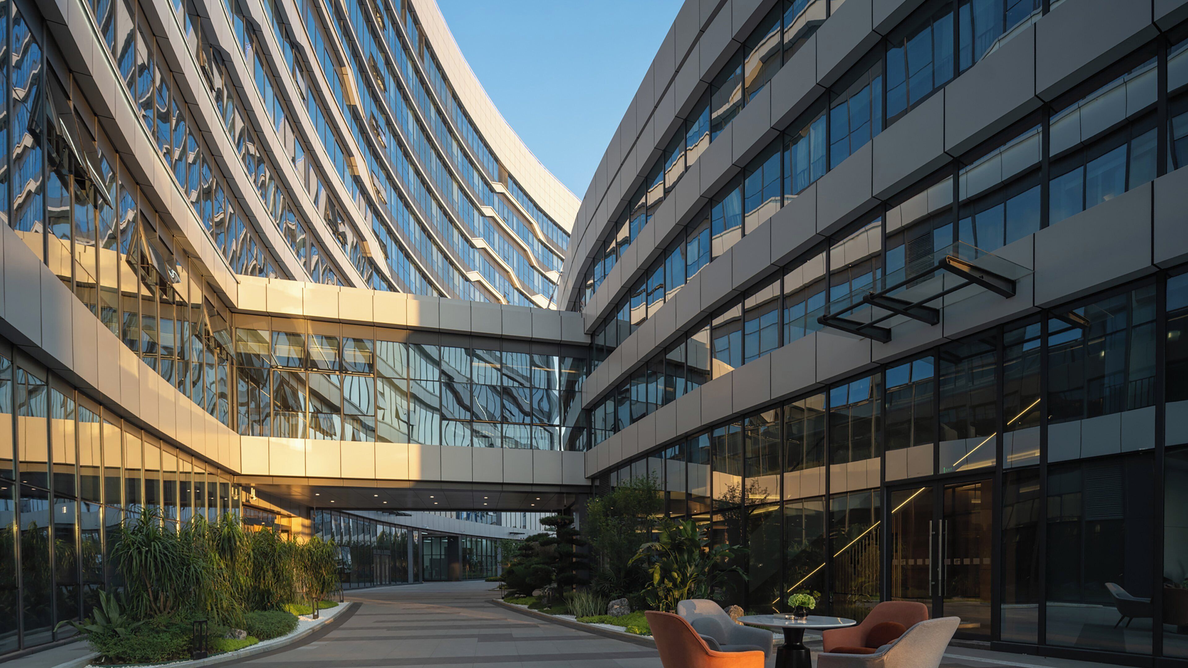 Un bâtiment moderne doté d’une façade incurvée, de grandes fenêtres et d’un espace extérieur aménagé pour s’asseoir.