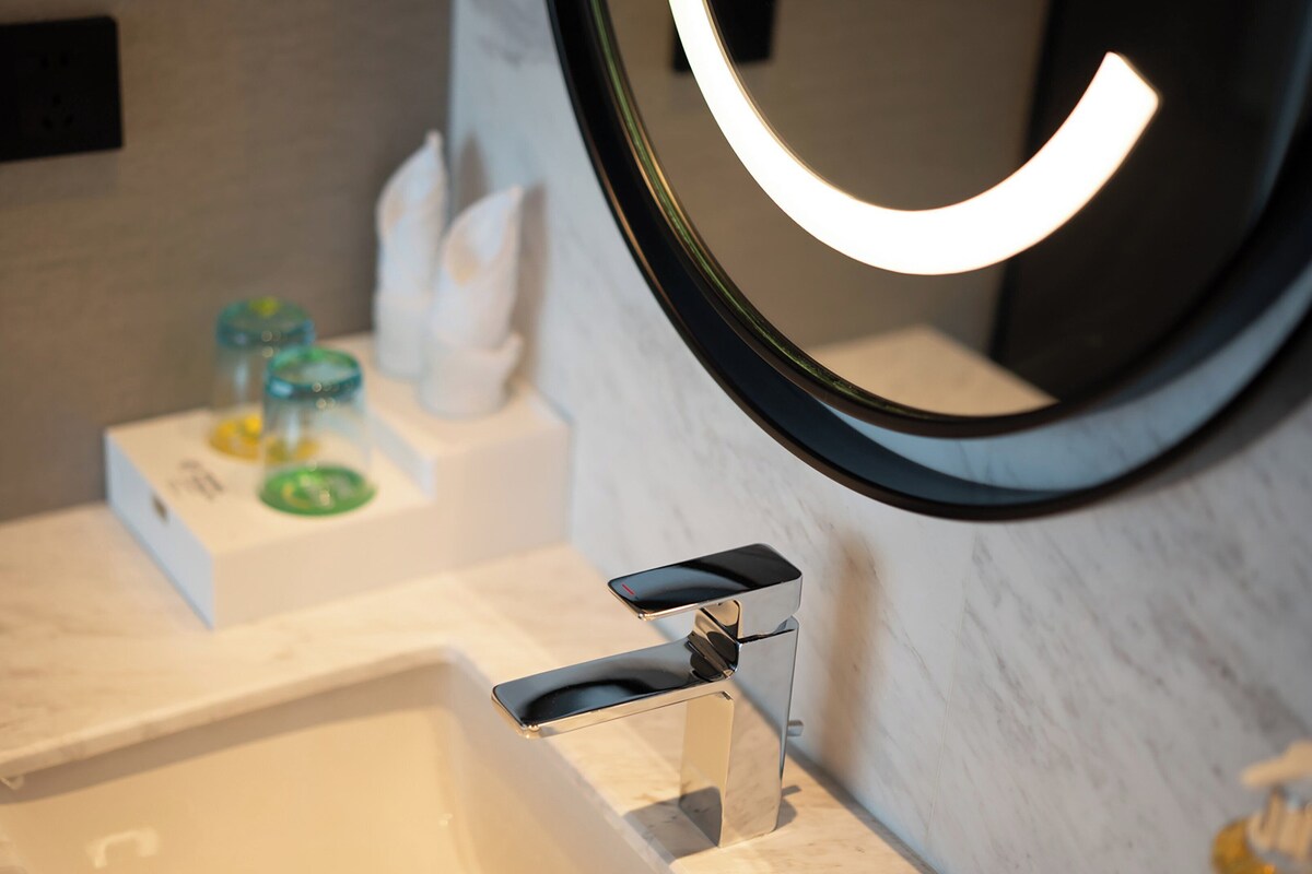 Un baño con un lavamanos blanco, un espejo de marco curvo e iluminación en la pared.