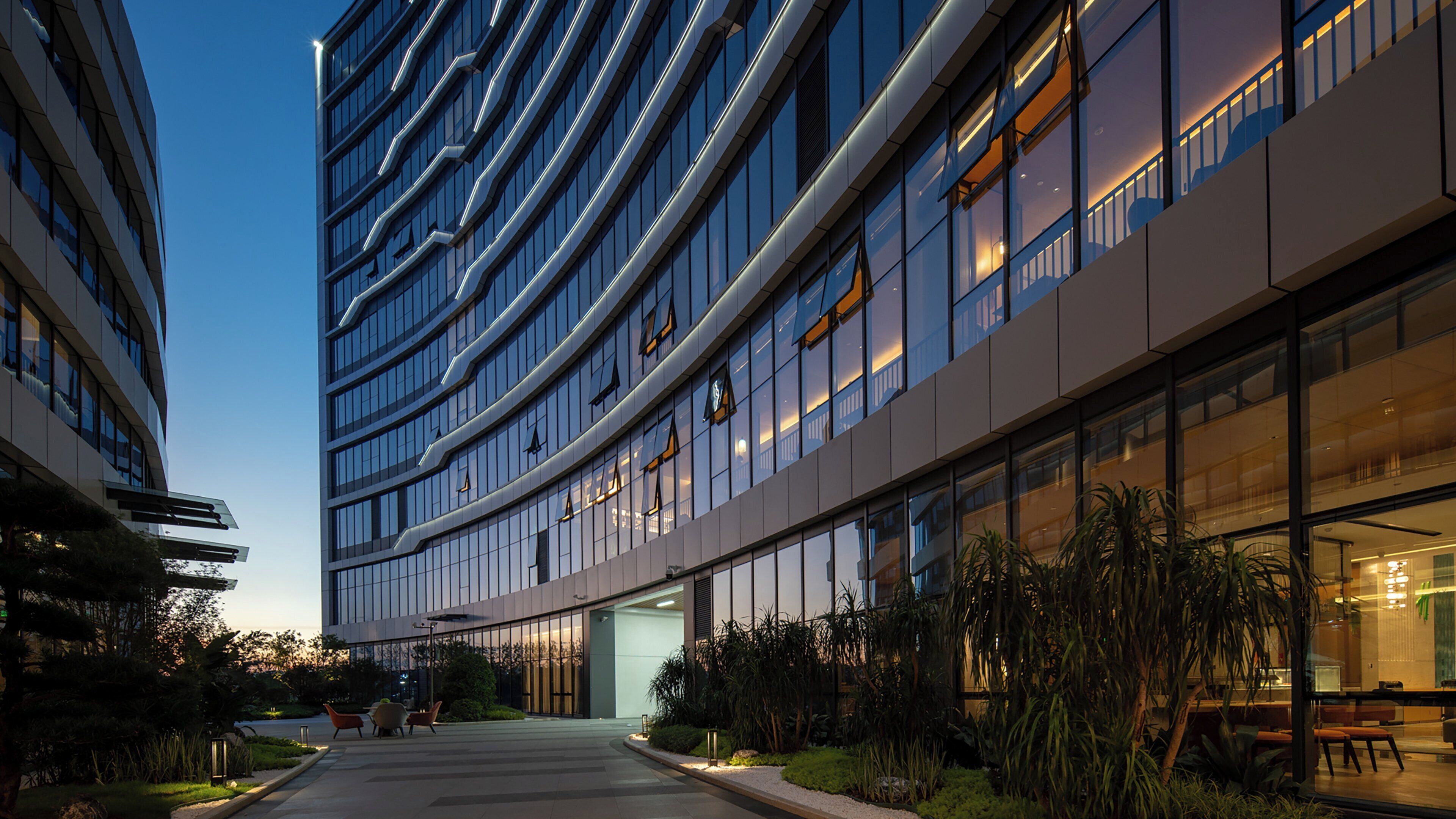 A modern building with a curved facade, large windows, and a well-maintained outdoor area with seating and plants.