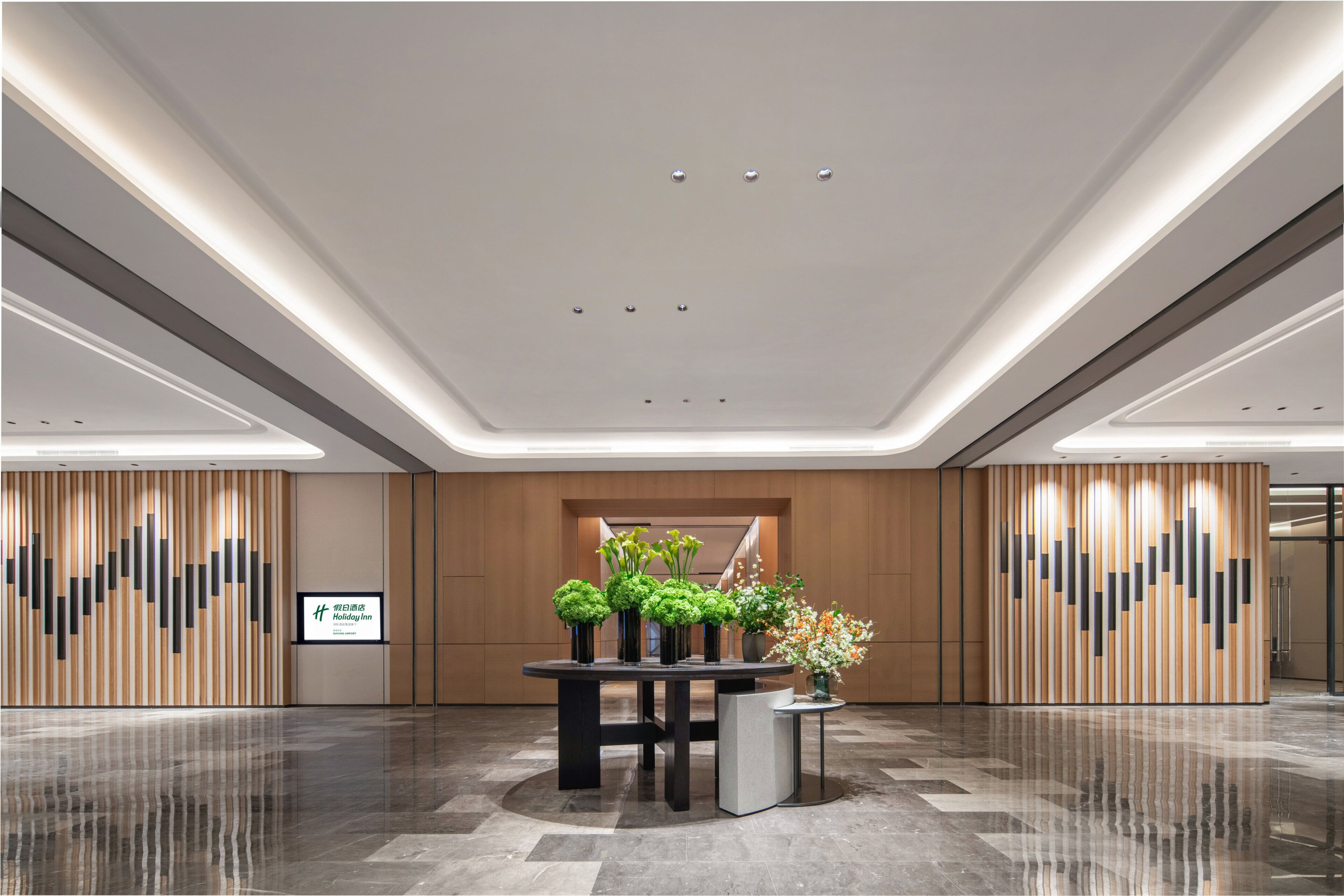 Un hall d’hôtel moderne avec un comptoir d’accueil, des plantes en pot et un panneau indiquant l’emplacement.