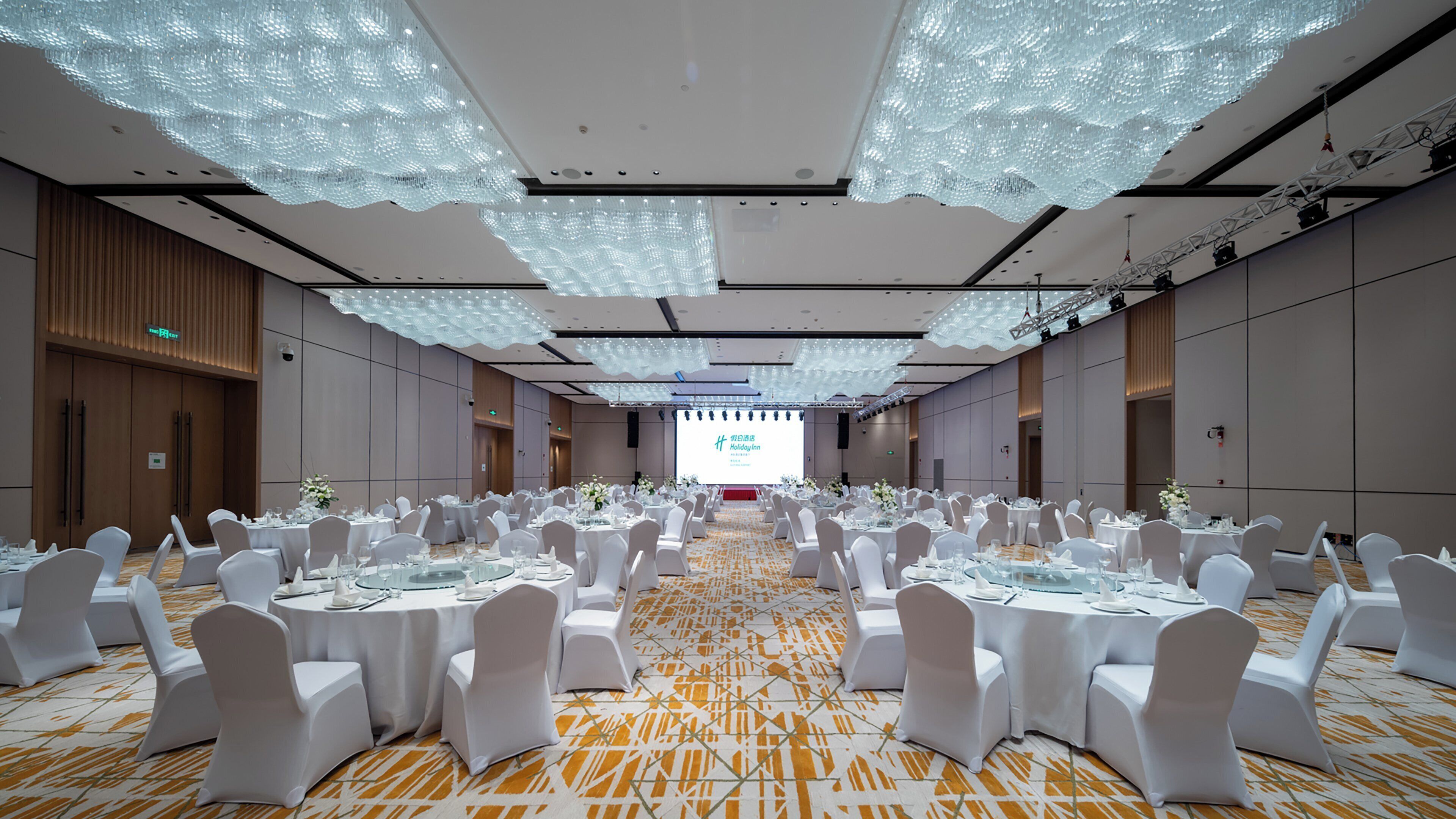 A conference room with round tables, white chairs, and a large screen at the front.