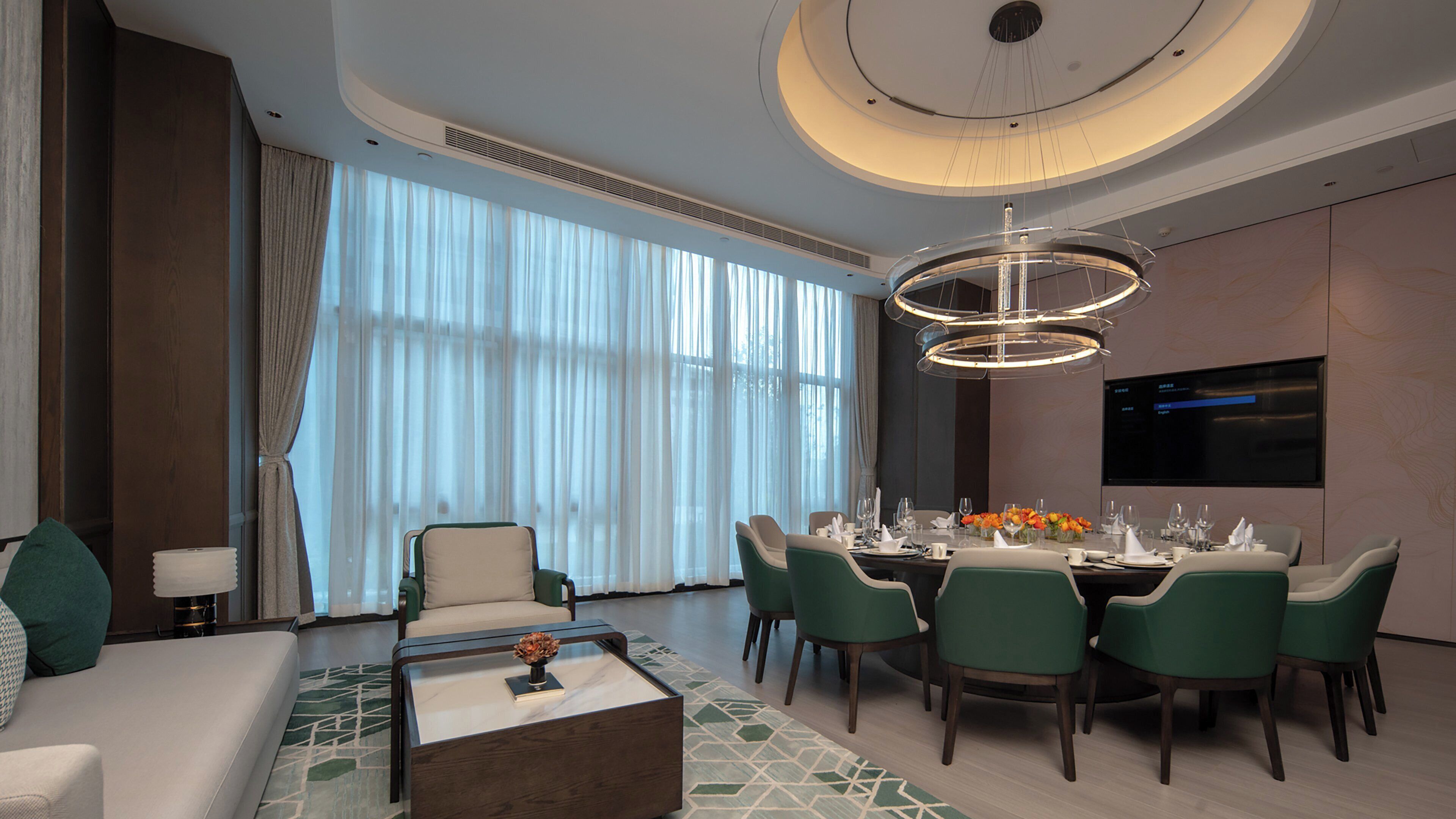 A modern dining room with a round table, green chairs, and a chandelier.