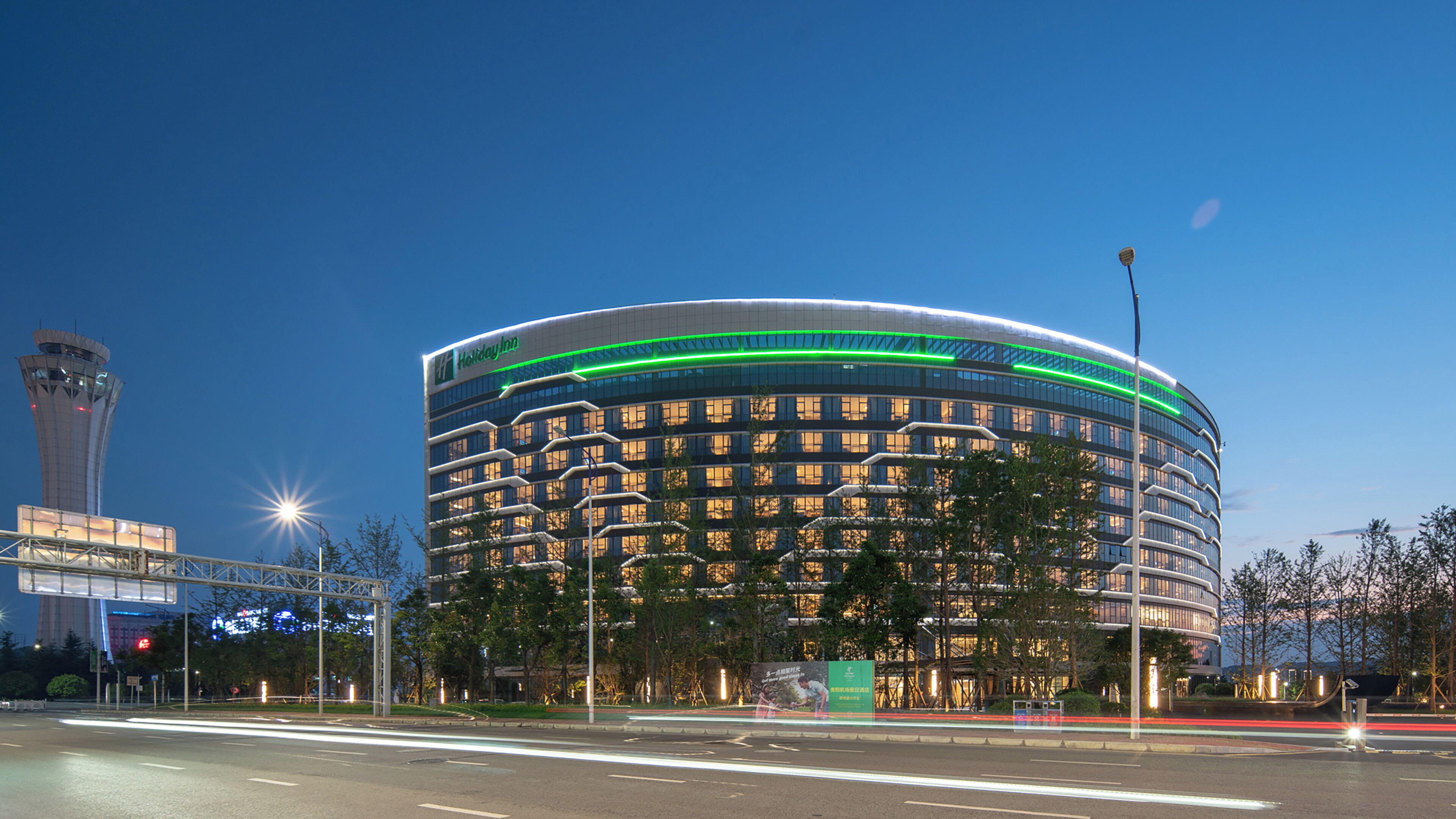 Ein modernes Hotel mit einer geschwungenen Fassade, mehreren Etagen und einem markanten Turm im Hintergrund.