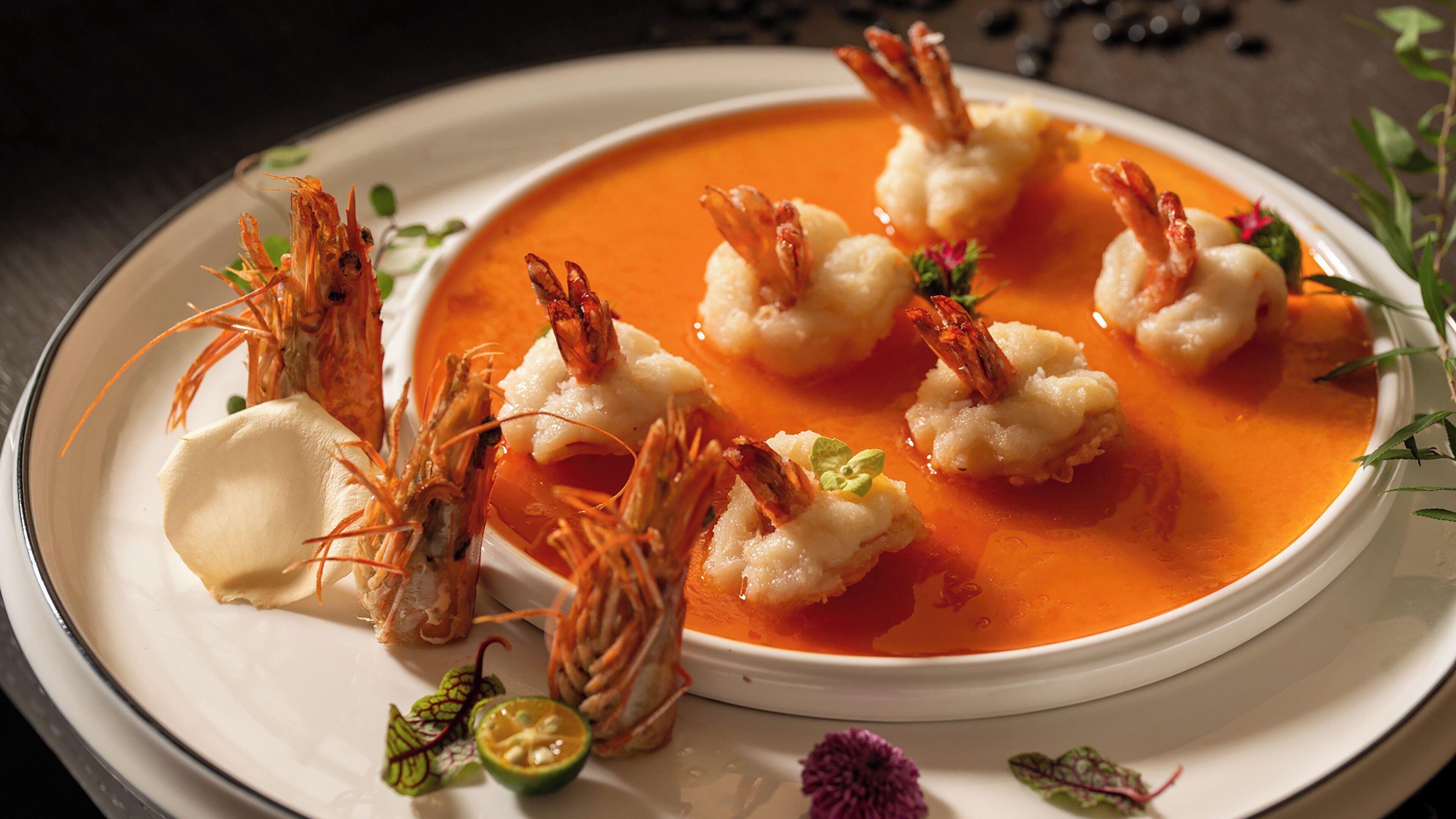 A bowl of soup with shrimp and a dollop of cream on a plate.