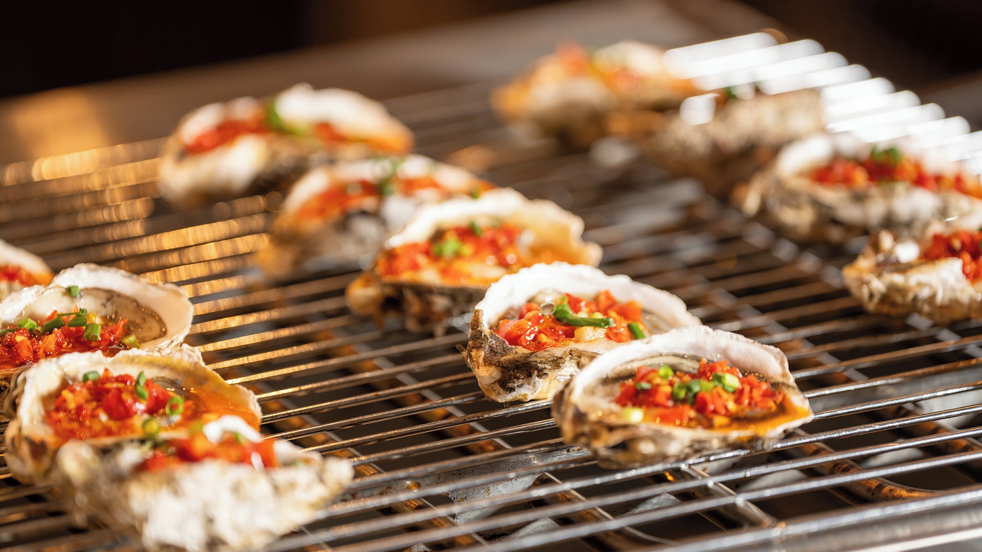 Grilled oysters with a topping on a grill.
