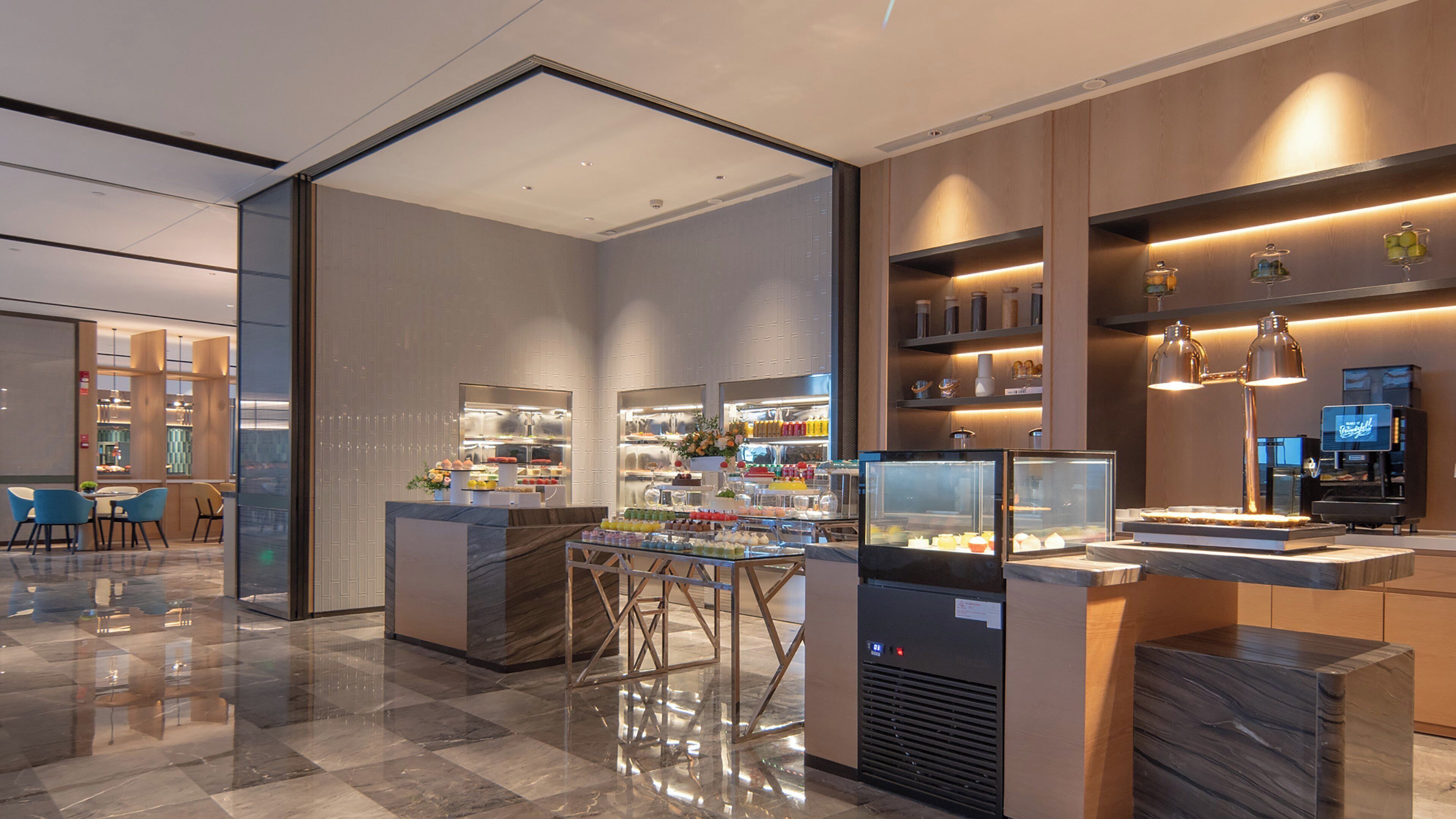 A modern hotel lobby with a check-in counter, seating area, and a glass partition separating the lobby from the dining area.