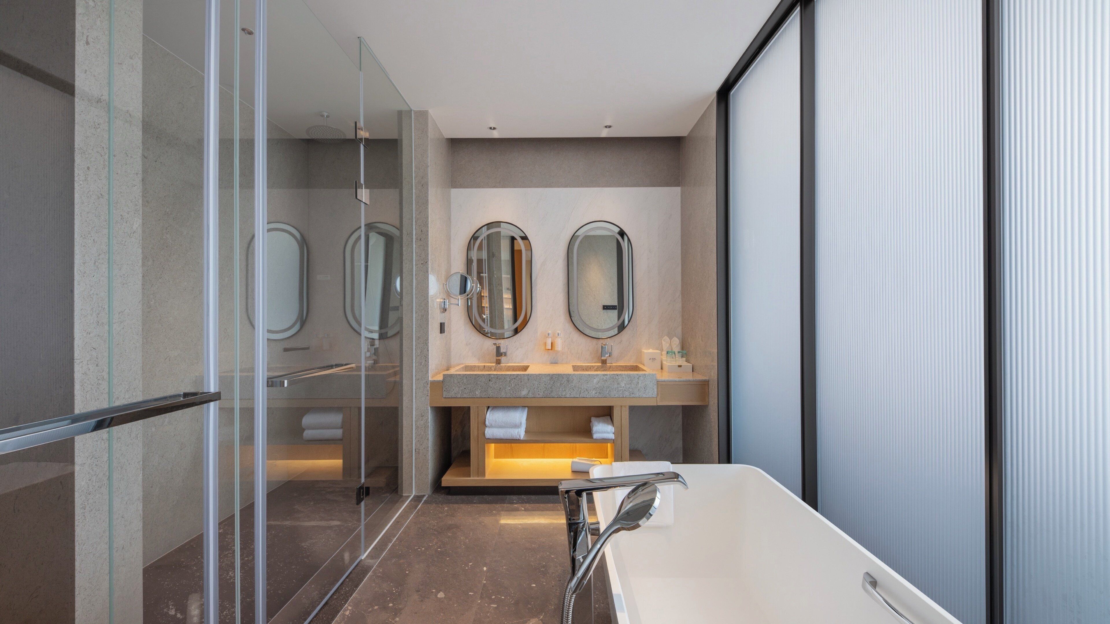 A modern bathroom with a glass shower enclosure, a double sink vanity, and a large bathtub.