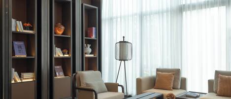 A modern living room with a sofa, armchairs, a coffee table, and a floor lamp. There are bookshelves filled with books and decorative items.
