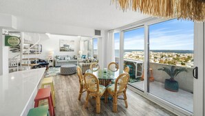 Un moderno salón con una mesa de comedor de vidrio, sillas de mimbre y vistas a la ciudad.