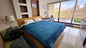 Habitación de hotel con una cama grande, un escritorio con lámpara, una silla y vistas al exterior.