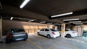 Un aparcamiento con tres coches estacionados en plazas marcadas, pilares de hormigón con letras y luces fluorescentes.