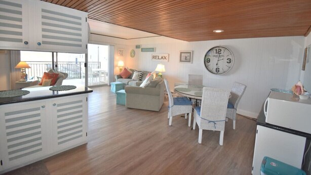 Ein gemütliches Hotelzimmer mit Holzbalkendecke, einem Essbereich mit Tisch und Stühlen, einer Couch und einer Küchenzeile mit Kühlschrank.