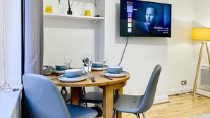 A dining area with a round table set for four, a flat-screen TV mounted on the wall, and a standing lamp to the right. - Cosy Hackney 1-bedroom Flat with Wi-fi, old street (London)