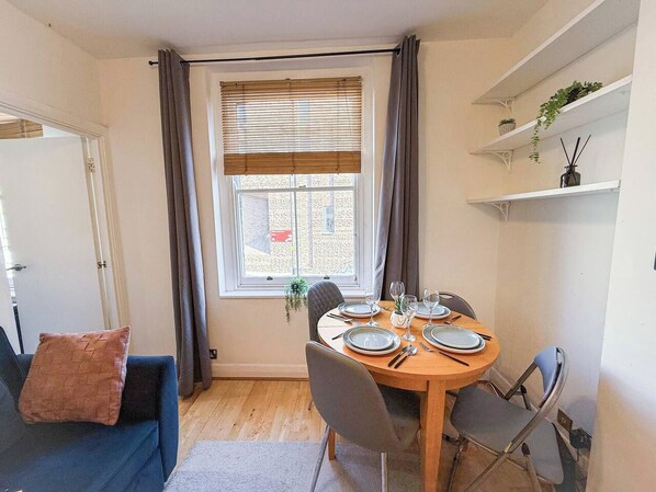 A dining area with a round table set for four, a blue sofa, and a window with curtains.