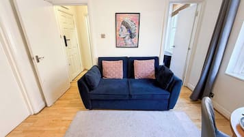 Ett vardagsrum med en mörkblå soffa, två rosa kuddar, ett inramat konstverk på väggen och en grå matta.