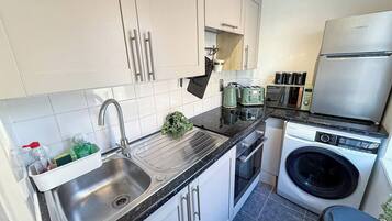 Een kleine keuken met een spoelbak, een broodrooster, een wasmachine en keukenkastjes.