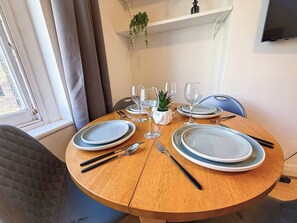 A round dining table set with plates, cutlery, and glasses, with a plant and a television above.