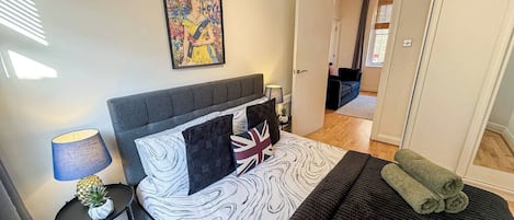Un dormitorio con cama, almohadas, una lámpara y un cuadro en la pared.