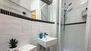 Un bagno con lavandino bianco, uno specchio, una doccia e una pianta in vaso.