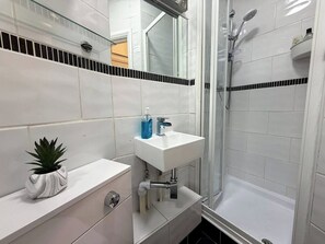 A bathroom with a white sink, a mirror, a shower, and a potted plant.