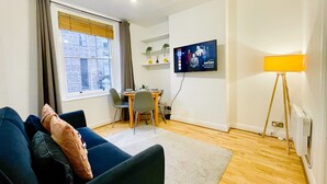 A modern living room with a sofa, dining table, and a flat-screen TV mounted on the wall. - Cosy Hackney 1-bedroom Flat with Wi-fi, old street (London)