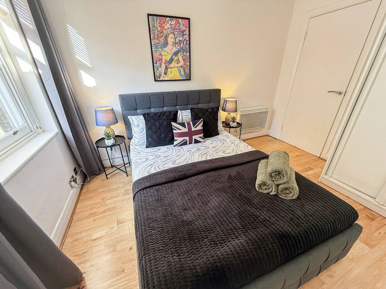 A bedroom with a bed, a bedside table, a lamp, a window, and a door.