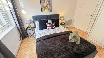 A bedroom with a bed, a bedside table, a lamp, a window, and a door.
