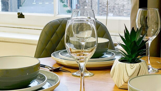A dining table set with plates, glasses, and cutlery, with a window view of a city street. - Cosy Hackney 1-bedroom Flat with Wi-fi, old street (London)