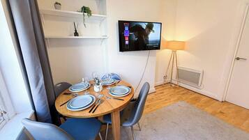 Ein Essbereich mit einem runden Tisch, gedeckt für vier Personen, einem an der Wand montierten Fernseher und einer Stehlampe.