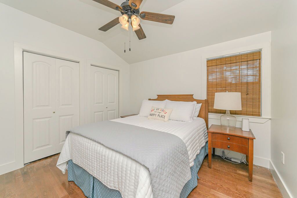 A bedroom with a bed, a nightstand, a ceiling fan, and a window with blinds.