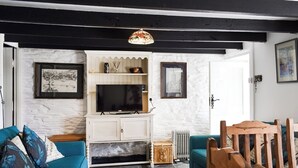 Ein Wohnzimmer mit einem blauen Sofa, einem Holzesstisch und einem Fernseher auf einem weißen Schrank.