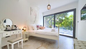 A bedroom with a white bed, a bedside table with a lamp, a bench, a dresser, and a large window with a view of greenery. - Wellness Villa- Four Bedroom Villa with Swimming pool (Grizane)