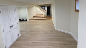 Un passadís amb terra de fusta, parets blanques i una escala que condueix a una altra habitació.