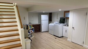 Una cuina moderna amb electrodomèstics blancs, una escala de fusta i un cubell de brossa.
