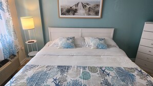 A neatly made bed with a blue and white coral pattern bedspread, a white headboard, and a framed picture of a beach scene above it. - Beautiful Ocean Views! Amazing Amenities! King Size Bed!  (Myrtle Beach)