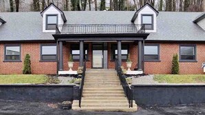 A two-story brick house with a front porch, a staircase leading to the entrance, and a small garden area.