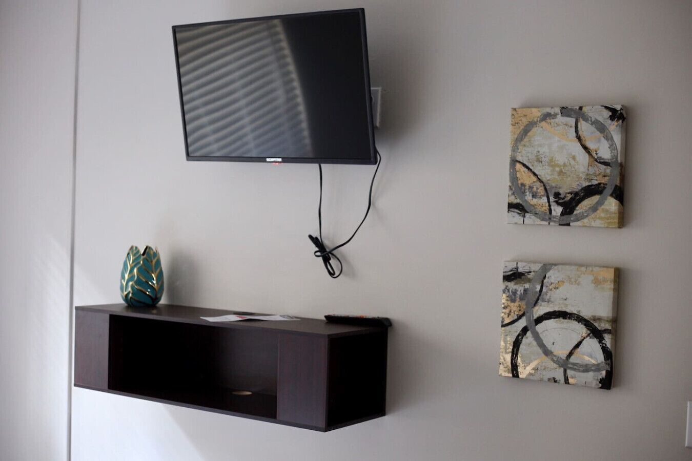 A flat-screen TV mounted on a wall, a dark wooden entertainment unit below it, and two abstract paintings on the wall.