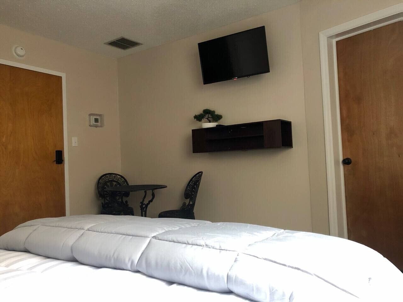 A bedroom with a bed, a TV mounted on the wall, a small table, and a chair.