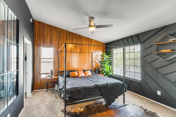 A modern bedroom with a bed, wooden panel walls, a ceiling fan, and large windows.
