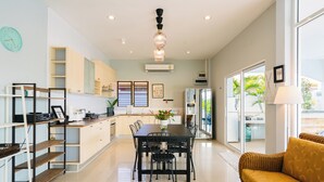 A modern kitchen with a dining area, featuring a large window, a sofa, and a chandelier.