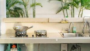 A kitchen with a gas stove, a sink, and a shelf with a bottle.