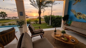 A terrace with a view of the sunset, outdoor seating, a pool, and a mural of a turtle.