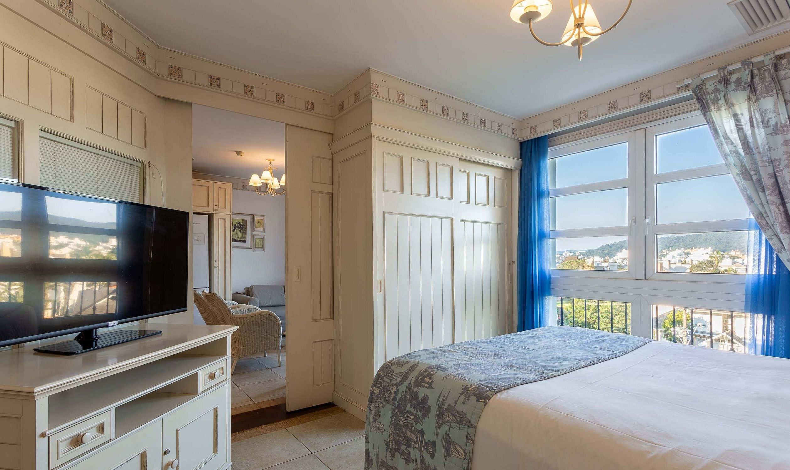 A bedroom with a TV, a bed, a dresser, and a window with a view.