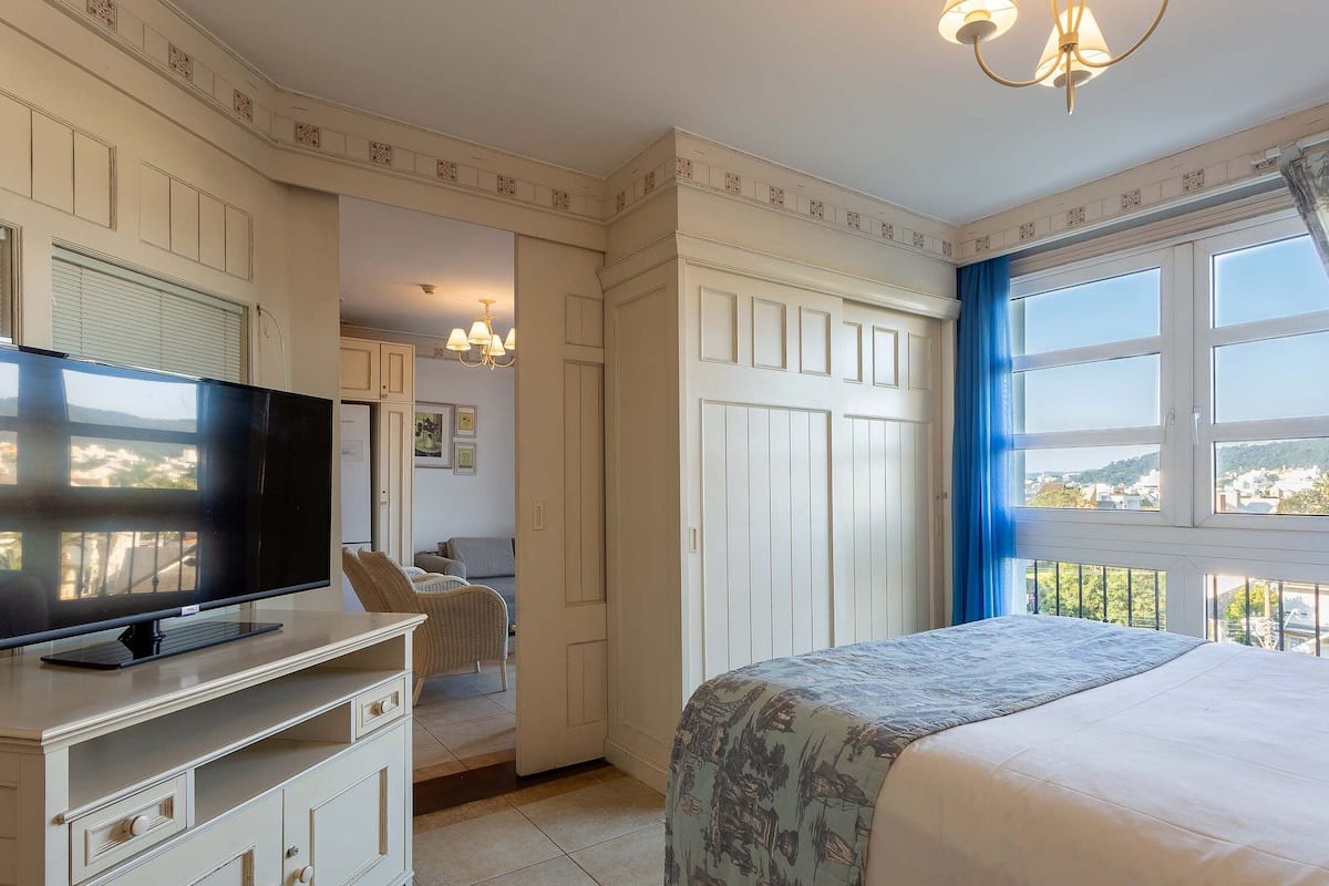Un dormitorio con cama, televisor sobre un mueble, armario y ventana con vistas.