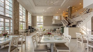 A spacious dining area with multiple tables and chairs, large windows, and a staircase leading to an upper level. - Studios frente ao mar no IL Campanario Resort ILCTOP (Florianópolis)