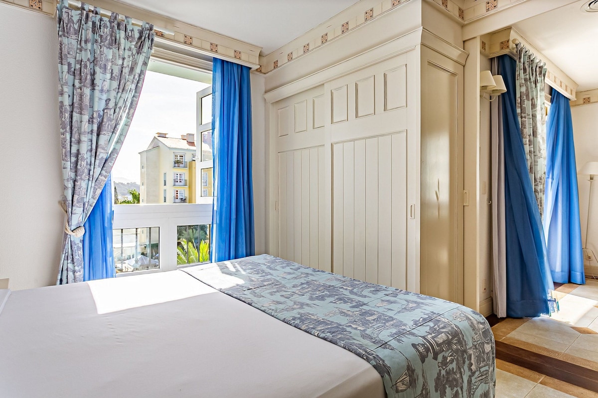 Un dormitorio con cama, cortinas, un armario y vistas a edificios.