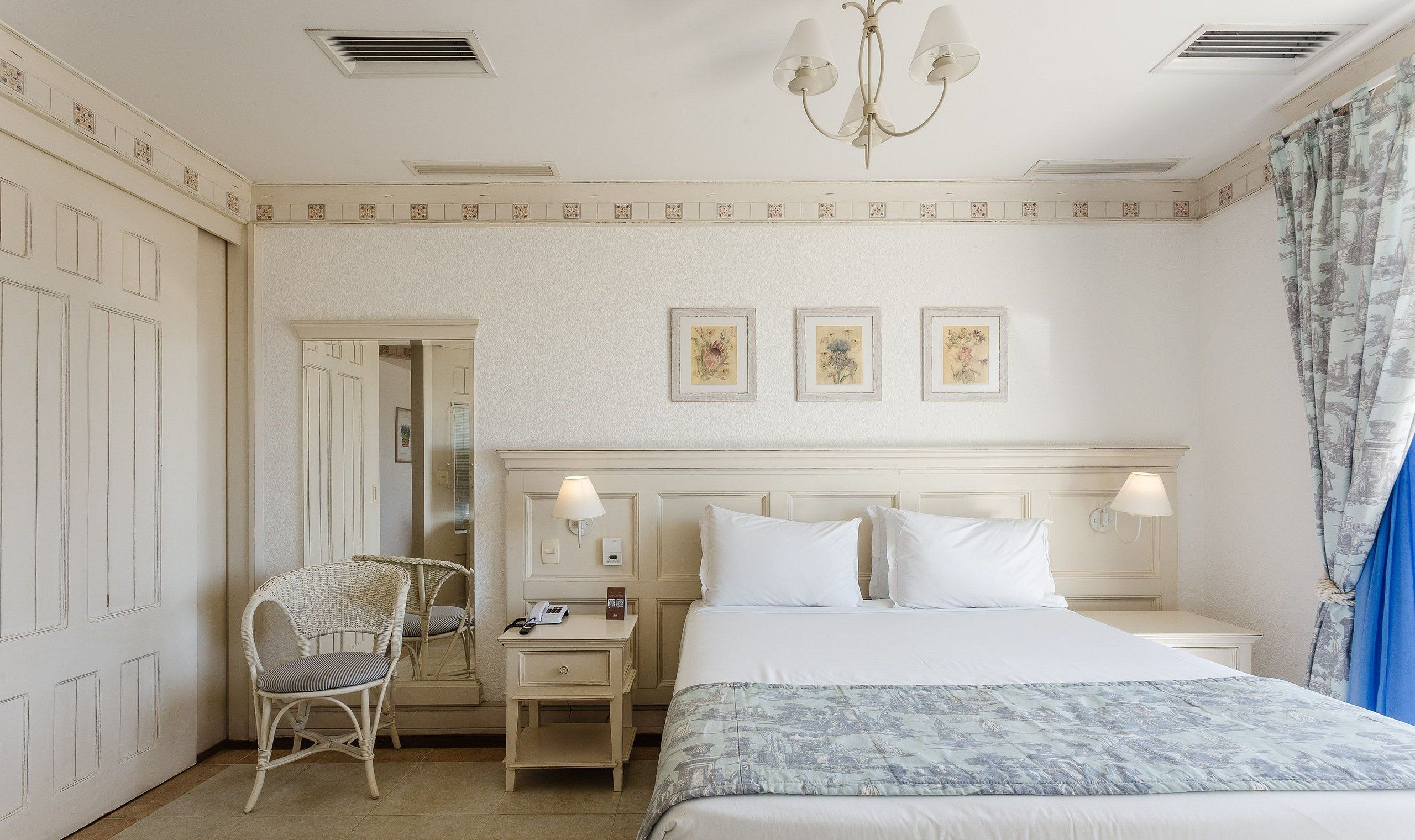 A hotel room with a bed, a nightstand, a chair, and a chandelier.