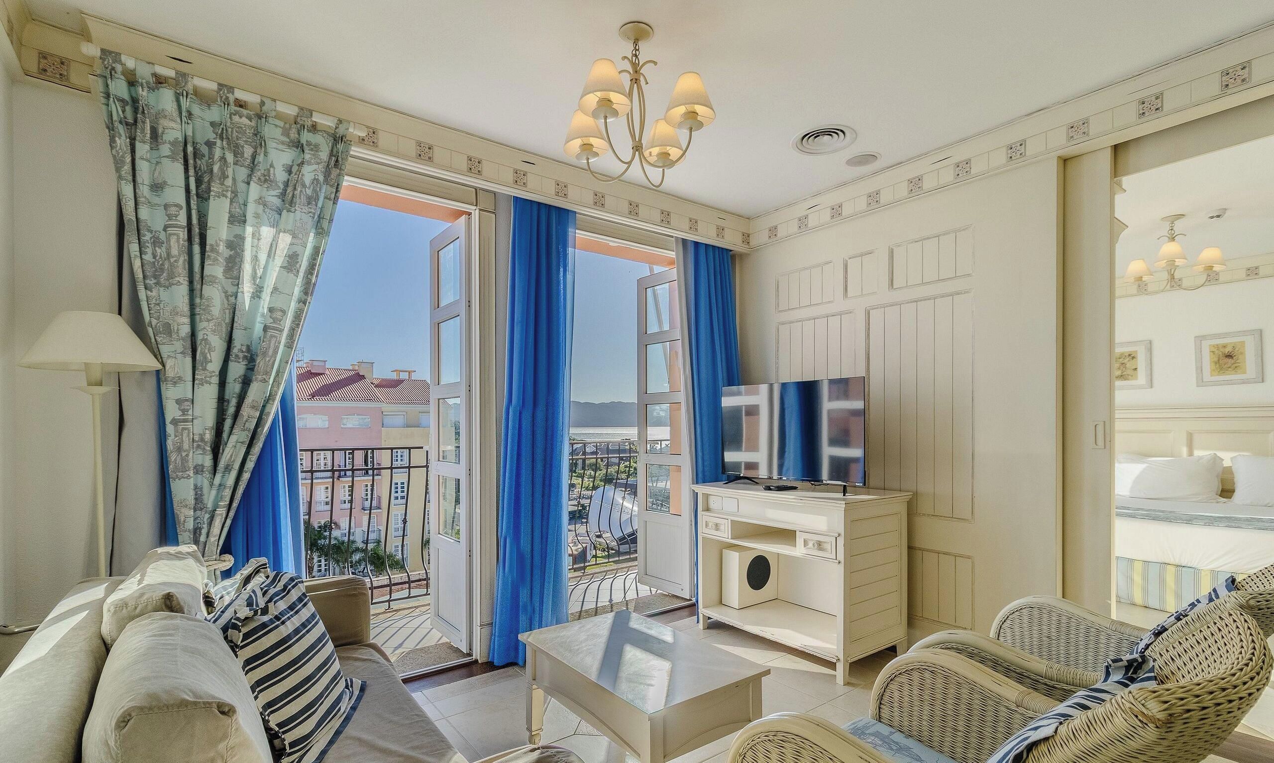 Habitación de hotel con sofá, televisión, una mesita y balcón con vistas a edificios.