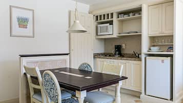 Un comedor con mesa y sillas de madera, una lámpara colgante y una cocina con muebles y electrodomésticos blancos.